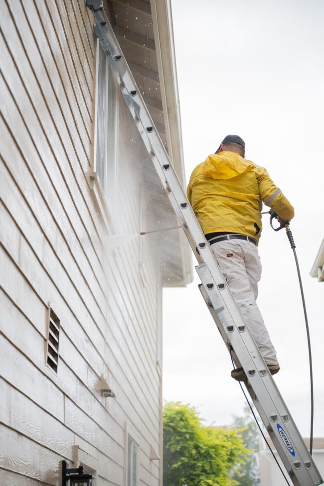 H.A. Painting crew member power washing the exterior of a house before applying a fresh coat of paint